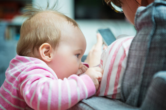 Ten months old baby girl trying to get her mother's attention; mother is sitting in a sofa texting messages on her smartphone