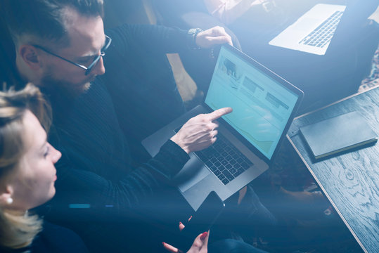 Coworking process in office.Two young colleagues using computer.Woman wearing black pullover and sitting on the sofa.Graphs and diagramm on laptop screen.Horizontal, visual effects.