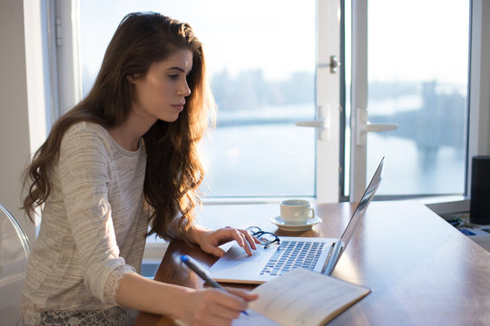 Young woman sits at her laptop with her day planner