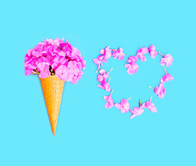 Ice cream cone with flowers and heart shape of petals over blue background top view