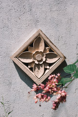 Rosette on the stone white wall with flowers, architecture of street of Asia