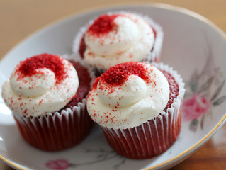 Delicious red velvet cupcakes decorated by vanilla frosting and red sugar on a top in a plate on a wooden table close up