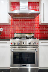 Modern designed kitchen with white cabinets, red back splash, stainless steel range oven and hood.