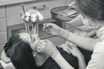 Black and white close up shot of Dentist at work examining woman's teeth in dental clinic