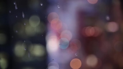 Rain drips down the window of a high rise building in a city. Shallow depth of field with bokeh