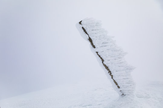Trekking sign pole on summit covered by heavy snow.