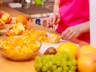 Obraz na płótnie Canvas Woman housewife in kitchen cutting orange fruits