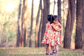 Two asian little girls having fun to play together in pine tree park in vintage color filter