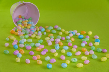 Jelly beans spilling out of a pink metal bucket on a green background
