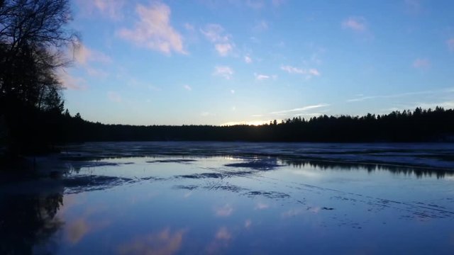 Mirroring lake, Zoom out time lapse of evening sky clouds mirroring on a icy lake, in siikajärvi, of Nuuksio national park, in Finland