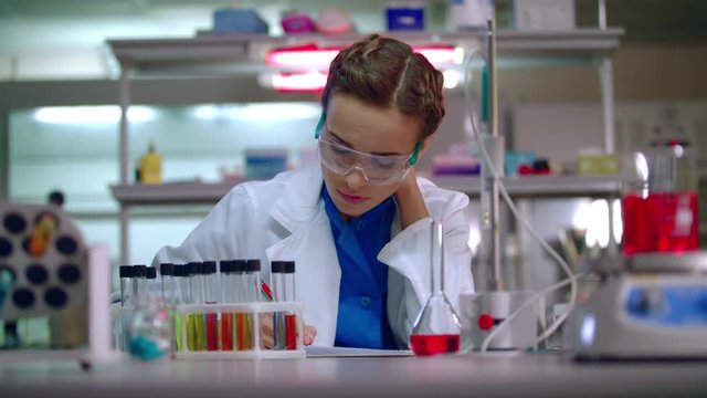 Woman researcher working in lab. Female researcher writing research report in modern laboratory. Woman scientist writing data report in research laboratory. Scientist woman working in chemical lab