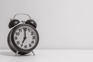 Closeup alarm clock for decorate in 7 o'clock on white wood desk and cream wallpaper textured background in black and white tone with copy space