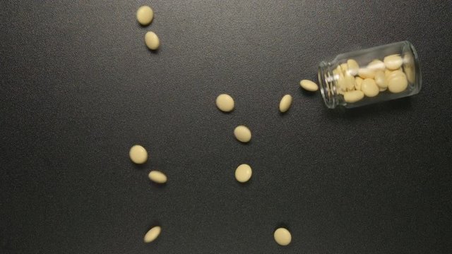 TOP VIEW: Glass jar falls and yellow pills fall out of him (slow motion)