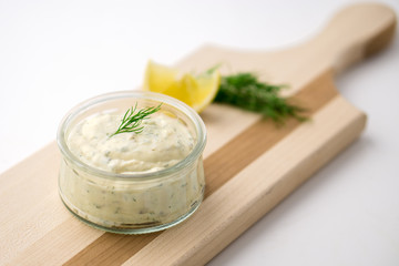 Tartar sauce on a wooden serving board. Made of fresh mayonnaise, lemon and various herbs. This classic creamy sauce is delicious with deep fried fish, seafood and many other dishes.