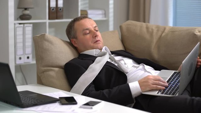Tired middle-aged businessman is sleeping on the sofa at the office.