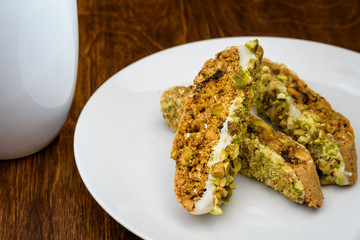 Homemade biscotti on a white plate, with a white coffee cup on a wood table
