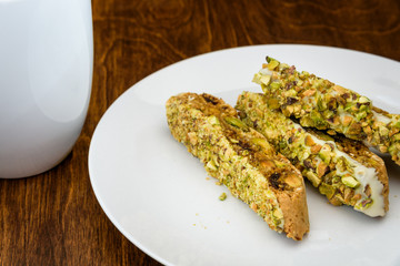 Homemade biscotti on a white plate, with a white coffee cup on a wood table
