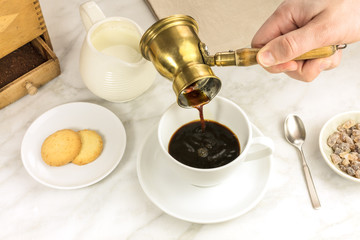 Coffee poured into cup, with milk jar and cane sugar