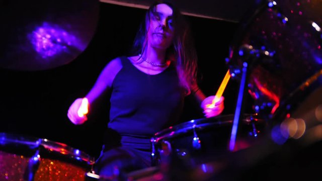Young woman playing electronic drums on stage. Concert - red Neon light.