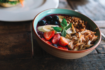 The bowl with smoothie, muesli, fruits and berries on the wooden table