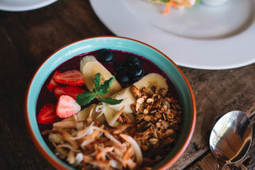 The bowl with smoothie, muesli, fruits and berries on the wooden table