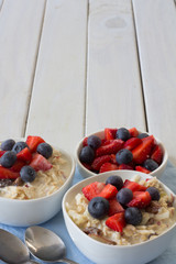 Two bowls of Bircher Muesli with Fresh Strawberries and Blueberries on Top with Copy Space Vertical