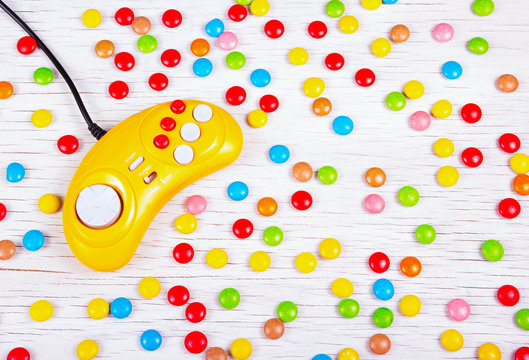 Yellow retro gamepad on a background of chocolate colored pills. Video game console GamePad on a white wooden table.