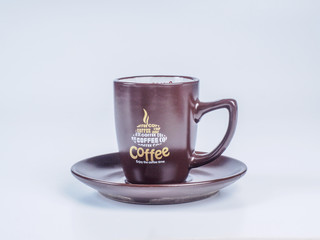 Close up on dark brown coffee cup standing on a saucer isolated on white background. Side view.