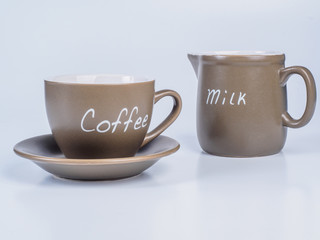 Close up on light brown coffee cup near milk can isolated on white background. Side view.