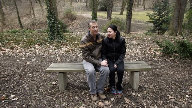 A male and female middle age couple spending quality time together and talking on a park bench enjoying their romantic time with each other during a day in early spring.