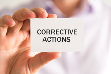 Businessman holding a card with CORRECTIVE ACTIONS message
