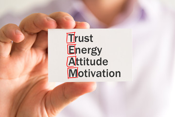 Businessman holding a card with TEAM TRUST ENERGY ATTITUDE MOTIVATION message