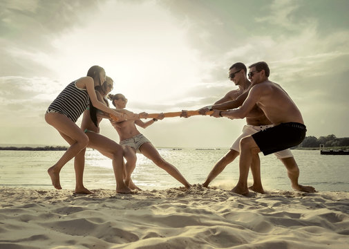 Friends funny tug of war on the beach under sunset sunlight.
