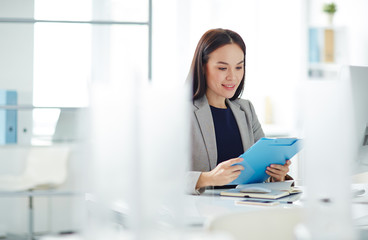 Portrait of successful Asian businesswoman busy working at desk in modern office, sorting folders...