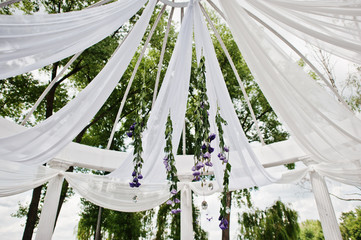 Decoration of wedding arch with violet flowers and white cloth outdoor.
