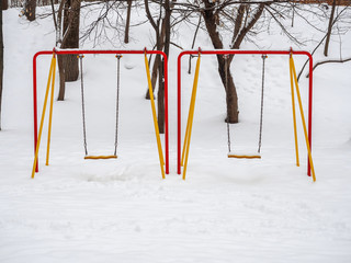 Multicolored snow-covered swing for children in the park in winter.