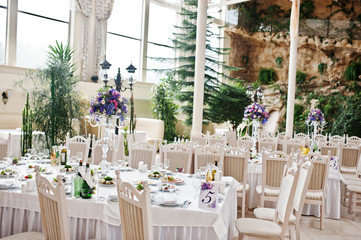 Awesome wedding hall with white chairs and purple flowers on tables.