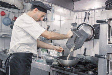 chef transferring pasta pan, commercial kitchen