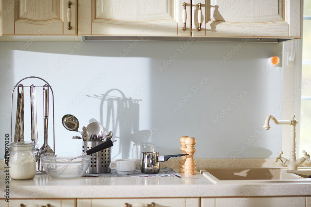 Wall mural preparations for cooking delicious pie: big glass bowl, whisk and flour jar standing on beige stone 