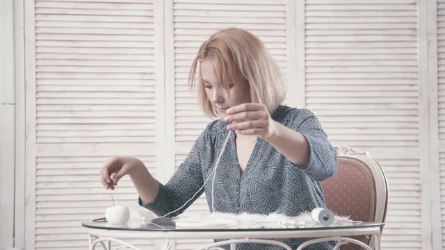 Young girl sitting at the table and making Dreamcatcher with bright feathers. Master makes new Dreamcatcher in art studio. Hobbies Crafts. Weaving dreams of thread catcher, feathers and beads.