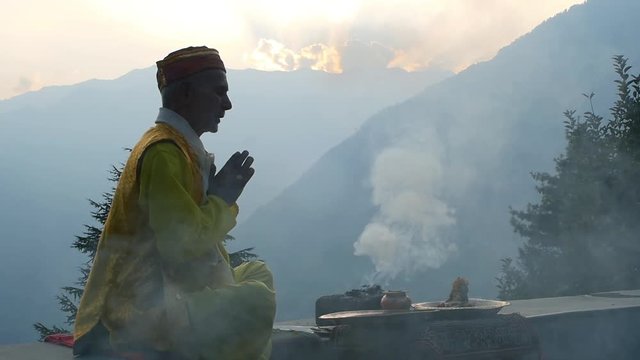 A Hindu old man in yellow national costume offering special spiritual prayer to god in the foothills of the Himalayas, Kullu Valley, India