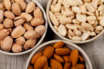 Pistachios, almonds, peanuts in ceramic plates. On the wooden table.