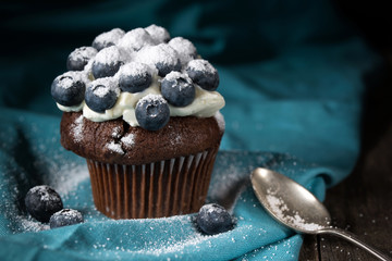 Chocolate muffin with soft cream and fresh blueberry powdered with sugar, rustic background