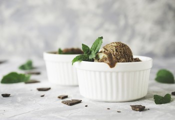 chocolate mint ice cream in white bowls with pieces of chocolate and mint leaves on a marble table