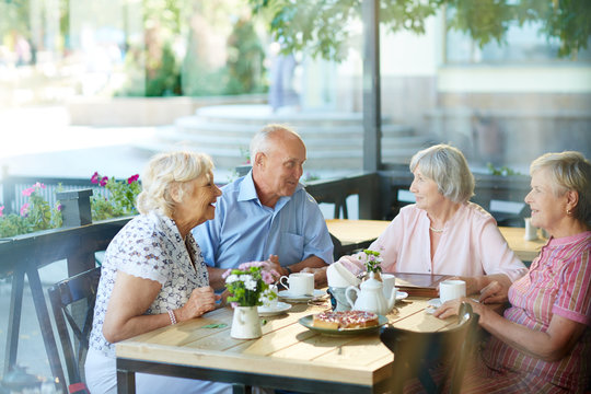 Four Childhood Friends Gathered Together In Outdoor Cafe After Long Separation And Remembering Funny Stories From Their Past