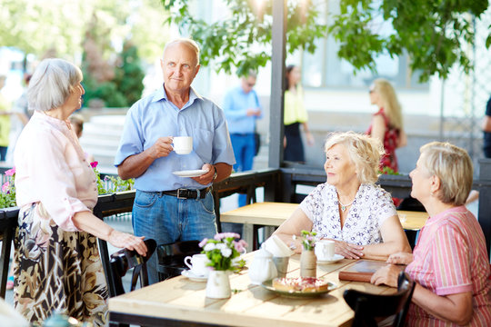 Group Of Senior Friends Enjoying Each Others Company In Summer Cafe And Drinking Tea With Berry Pie