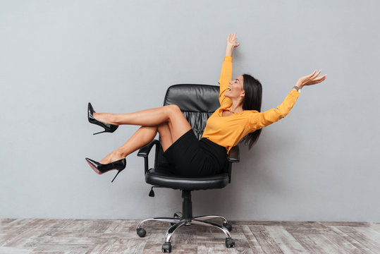 Happy business woman sitting on chair with raised arms