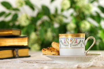 Beautiful cup of hot beverage with pastry and books on a vintage table in the garden