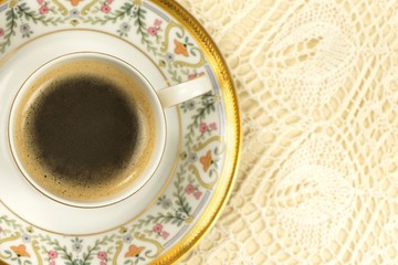 Romantic cup of coffee with foam on a vintage embroidered table cloth, top view