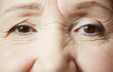 Smiling dark brown eyes of elderly woman looking at camera, extreme close-up shot